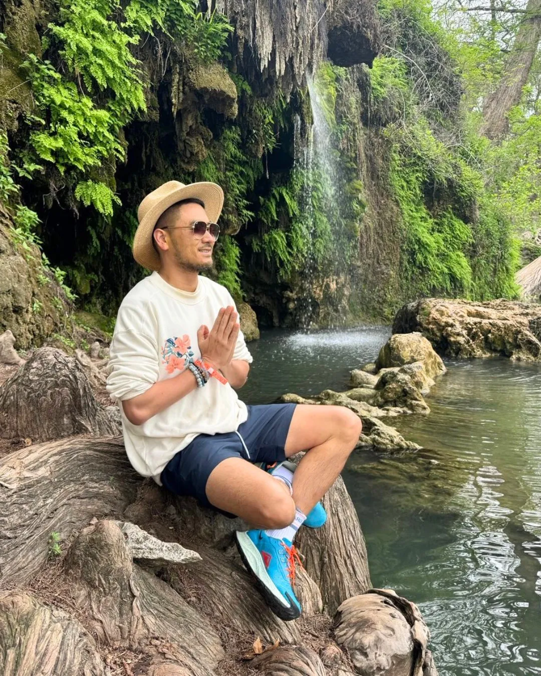 Patrick Chan sitting on a rock beside a waterfall, hands together