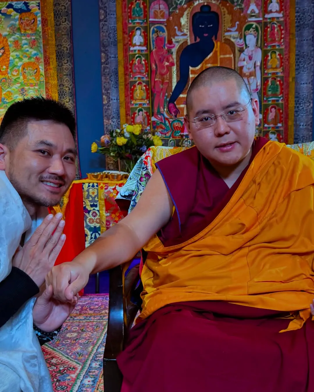 Patrick Chan kneeling beside a seated man in maroon and saffron robes